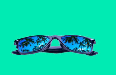 Sunglasses in a black frame with palm trees in the reflection of the lenses on a green background, isolated