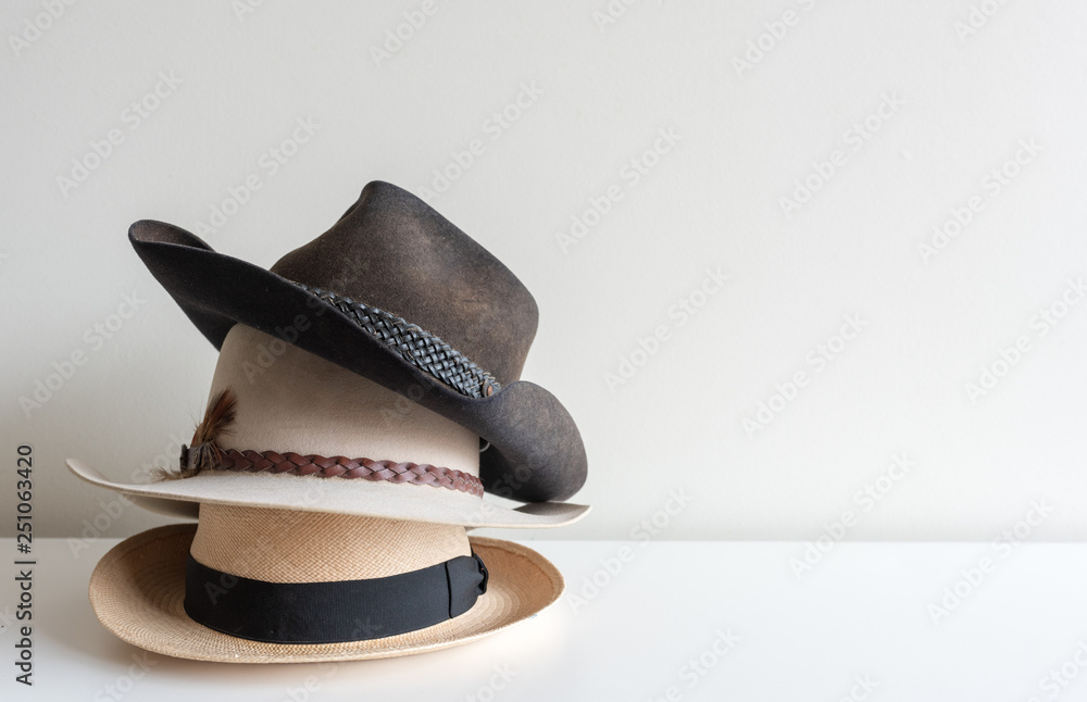 Three men's hats stacked on white shelf against neutral wall background with copy space - obrazy, fototapety, plakaty 