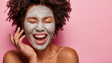 Cropped Image Of Cheerful Pleased Young African American Woman Has Deep Cleansing Nourishing Face Mask, Shows Bare Shoulders, Isolated Over Rosy Background With Blank Space For Your Promotion.