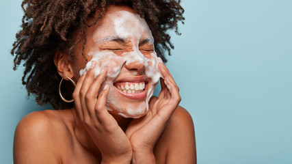 sideways shot of pleasant looking lady applies cosmetic foam, feels pleasure after beauty treatments