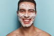 © wayhome.studio  - Skincare and morning routine concept. Positive man with soap scrub on face, enjoys relaxing time, shows bare shoulders, models over blue background, uses facial cleanser, shows perfect teeth