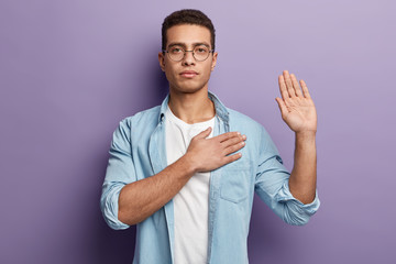 honest serious hipster guy swears to do something, keeps hand on chest, gestures with palm, promises