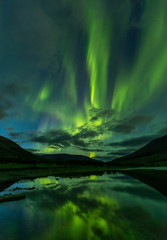 aurora borealis in the night sky cut the mountains, reflected in the water.