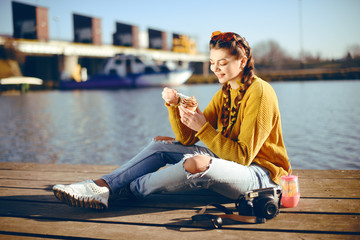 Wall Mural - The girl at hot sunny day eat ice cream. Summer vibes. Girl with fashion yellow sunglasses and dressed in yellow. Beautiful girl sitting on the pier near the river. Beauty model with brunette hair.