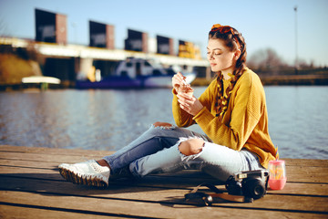 Wall Mural - The girl at hot sunny day eat ice cream. Summer vibes. Girl with fashion yellow sunglasses and dressed in yellow. Beautiful girl sitting on the pier near the river. Beauty model with brunette hair.