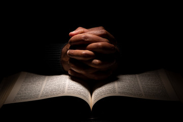 african american man praying with hands on top of the bible.