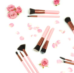 Makeup cosmetic accessories products .Professional make up brushes set  and pink roses on white background. Flat lay. Top view. 