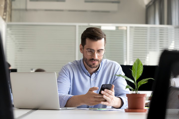 Focused businessman sitting at desk looking at cellular 