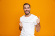 © Drobot Dean - Image of joyful man 30s with beard and mustache showing thumb up while standing, isolated over yellow background