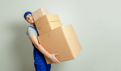 Wall Mural - Day moving. Delivery of goods from shopping in the online store. Loader or courier carries heavy cardboard boxes against gray wall