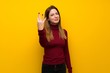 © luismolinero - Woman with turtleneck over yellow wall happy and counting three with fingers