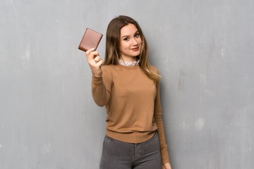 Teenager girl over textured wall holding a wallet