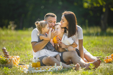 Wall Mural - Young family having picnic outdoor. Mother, father and their kids having fun in the park. Summer resting at the nature.