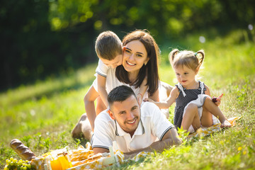 Wall Mural - Young family having picnic outdoor. Mother, father and their kids having fun in the park. Summer resting at the nature.