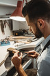 © Friends Stock - Made with love. Vertical photo of young male jeweler working and shaping an unfinished ring with a tool in workshop.