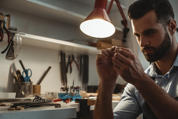 Perfection. Close up of young male jeweler looking and inspecting a ring.