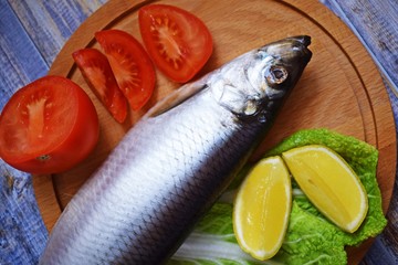 Delicious herring with lemon and tomatoes on lettuce leaves.