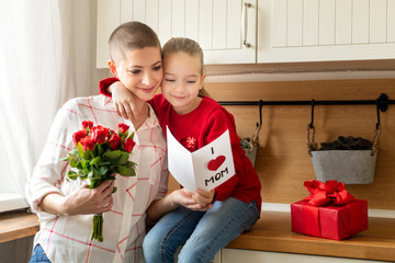 Adorable young girl and her mom, young cancer patient, reading a homemade greeting card. Family celebration concept. Happy Mother's Day or Birthday Background.