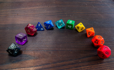 various colorful types of plastic polyhedral game dice arranged in a rainbow on a wooden table