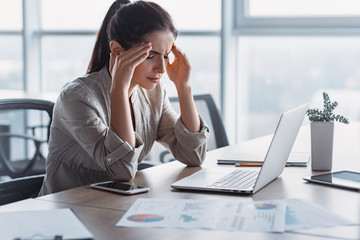 Young attractive woman at modern office desk. She has severe headache. Office syndrome concept