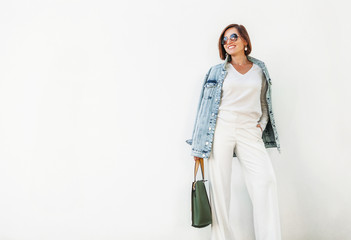 Posing woman in elegant white outfit with oversize denim jacket