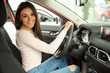 © Nestor - Gorgeous young girl sitting in automobile cabin, looking at camera and smiling. She testing comfortable seats and steering wheel. Beautiful female customer buying new car.