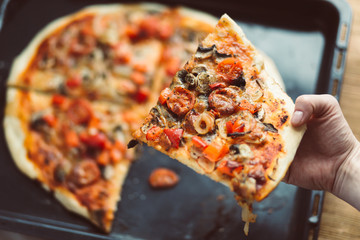 Piece of pizza held in the hands of a woman. Home made pizza served by hand. A snack at a home party. Shallow depth of field and instagram filter.