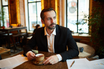 Wall Mural - Portrait of handsome businessman drinking coffee in cafe during break and looking away pensively, copy space