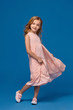 © nazarovsergey - Fashionable little girl in a pink dress is posing on a blue background.