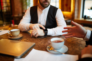 Wall Mural - Closeup of unrecognizable businessman pointing at wristwatch with blank screen during meeting in cafe, copy space