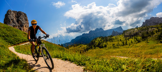 Tourist cycling in Cortina d'Ampezzo, stunning Cinque Torri and Tofana in background. Man riding MTB enduro flow trail. South Tyrol province of Italy, Dolomites.