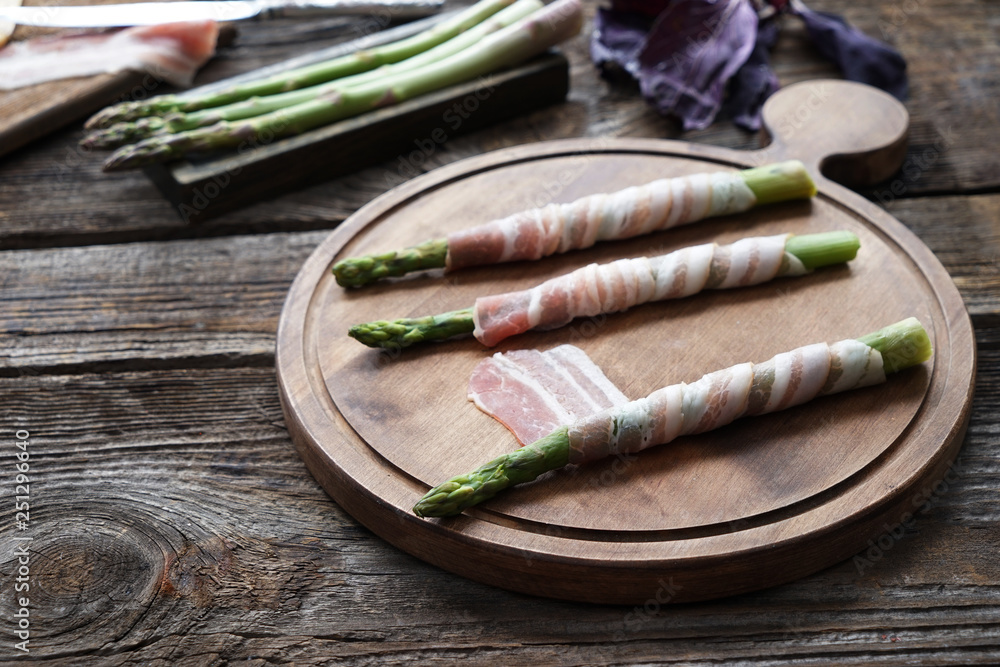 Board with bacon wrapped asparagus on wooden table