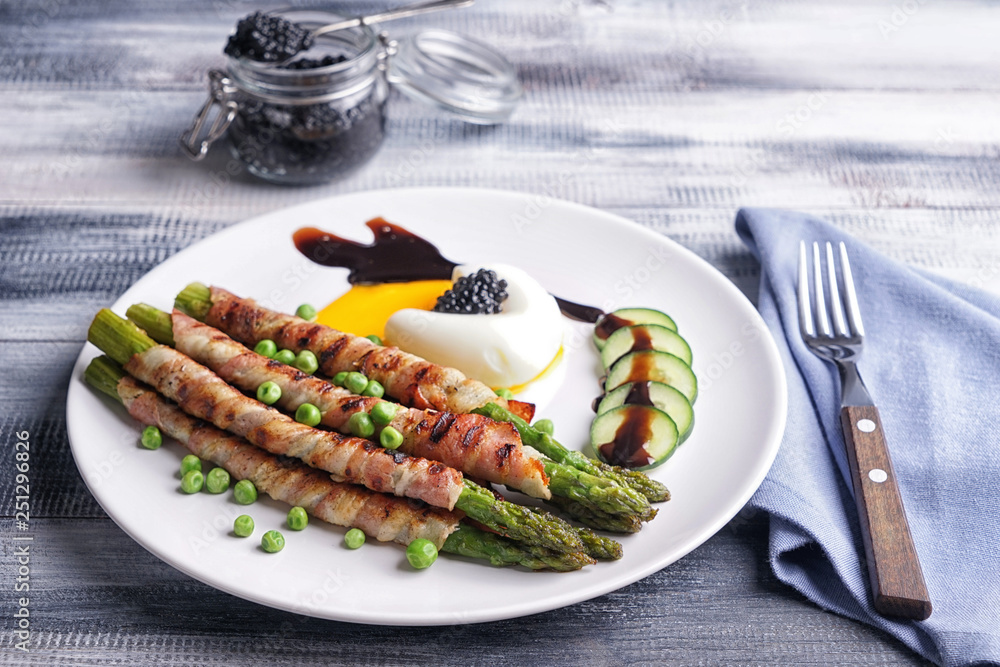 Plate with bacon wrapped asparagus and egg on wooden table