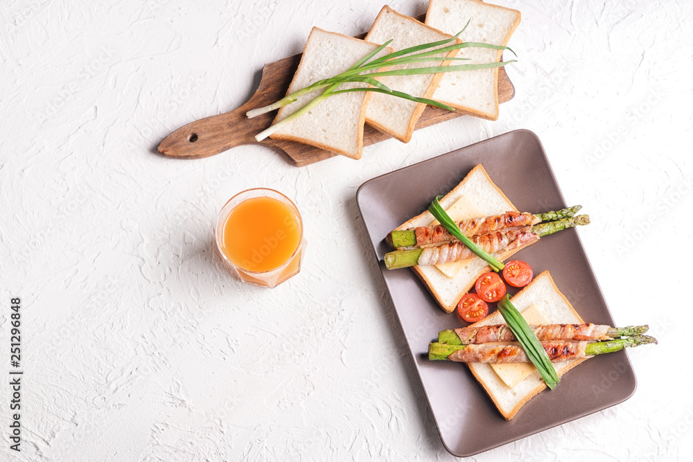 Plate with bacon wrapped asparagus and bread on white table