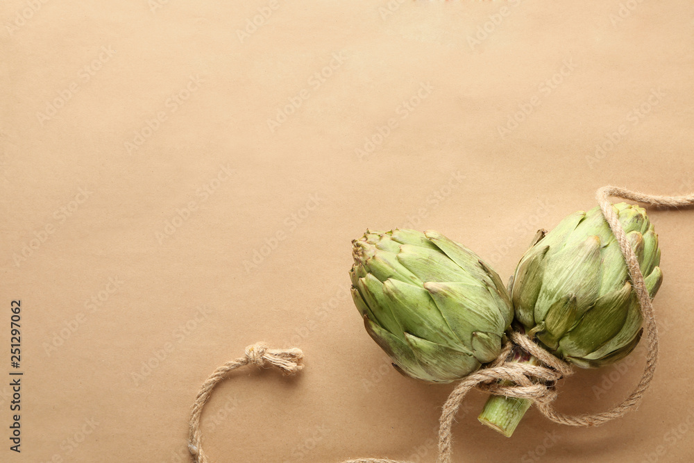 Tasty raw artichokes with rope on paper background
