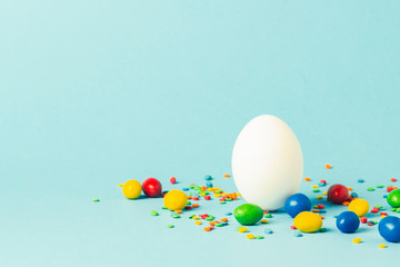 Wall Mural - White Easter egg and multi-colored sweets on a blue background. Easter celebration concept