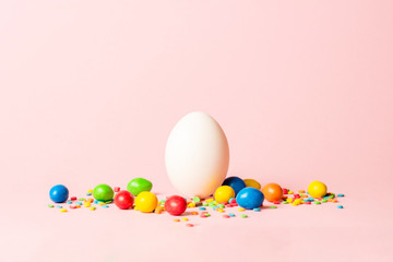 Wall Mural - White Easter egg and multi-colored sweets on a pink background. Easter celebration concept