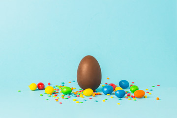 Wall Mural - Chocolate Easter egg and multi-colored sweets on a blue background. Easter celebration concept