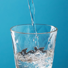 Wall Mural - water is poured into a glass cup, on a blue background