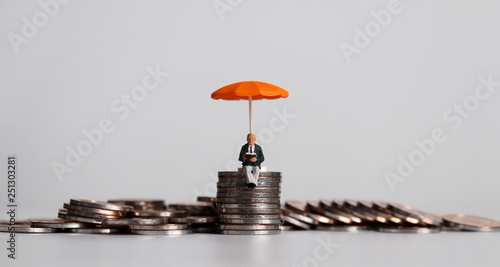 Cuadros en Lienzo Stack of coins and a miniature people with a orange umbrella.