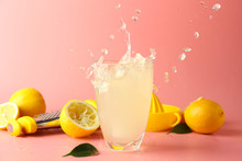 Glass of tasty cold lemonade with splashes on color background
