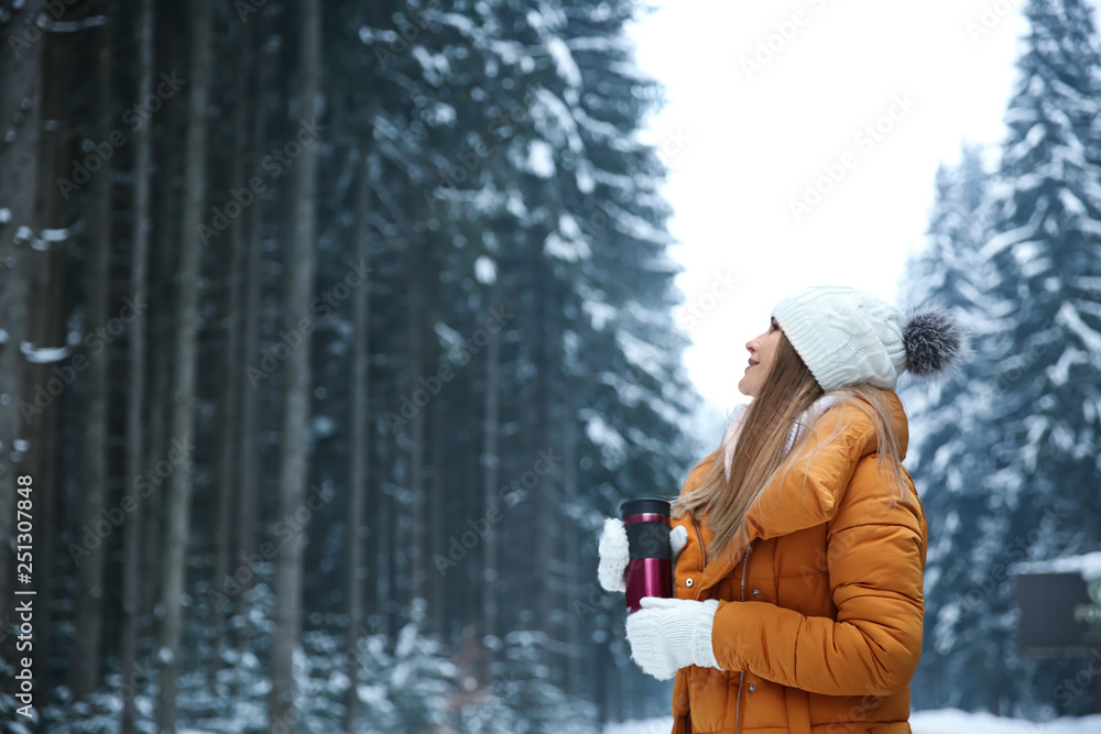 Beautiful young woman with hot drink in winter forest
