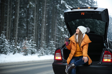 Wall Mural - Young woman with hot drink near car at winter resort