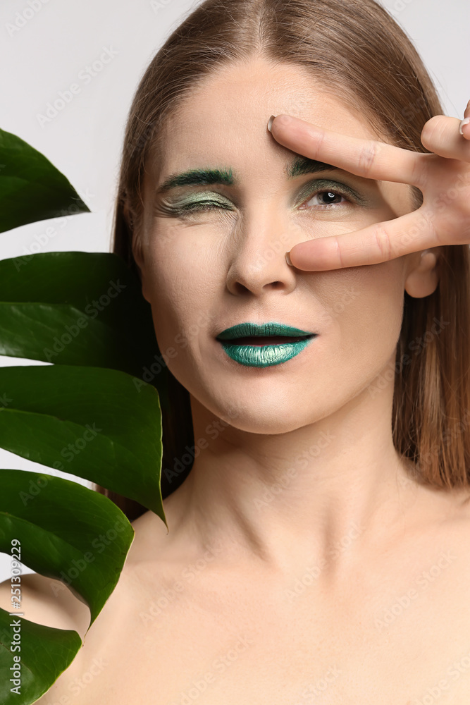 Beautiful woman with unusual makeup and tropical leaf on white background