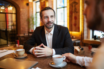 portrait of handsome mature businessman talking to partner during meeting in cafe, copy space