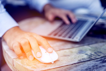 Businessman hand holding computer mouse with laptop keyboard in the co-workspace.