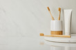round board with toothpaste in tube, holder and bamboo toothbrushes on white marble background