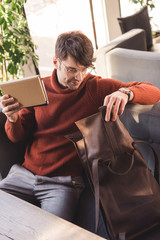 cheerful man in glasses holding books and looking at bag in cafe