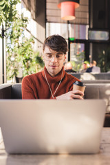 Sticker - selective focus of man listening music in earphones while using laptop and holding paper cup in cafe