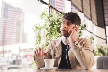 Wall Mural - man holding spoon near cup with cappuccino and talking on smartphone in cafe